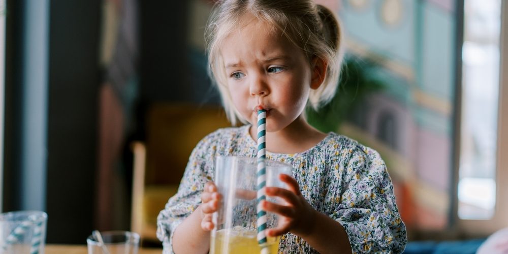 Little,Girl,Drinks,Juice,From,A,Glass,Through,A,Straw Cannucce biodegradabili per mense scolastiche