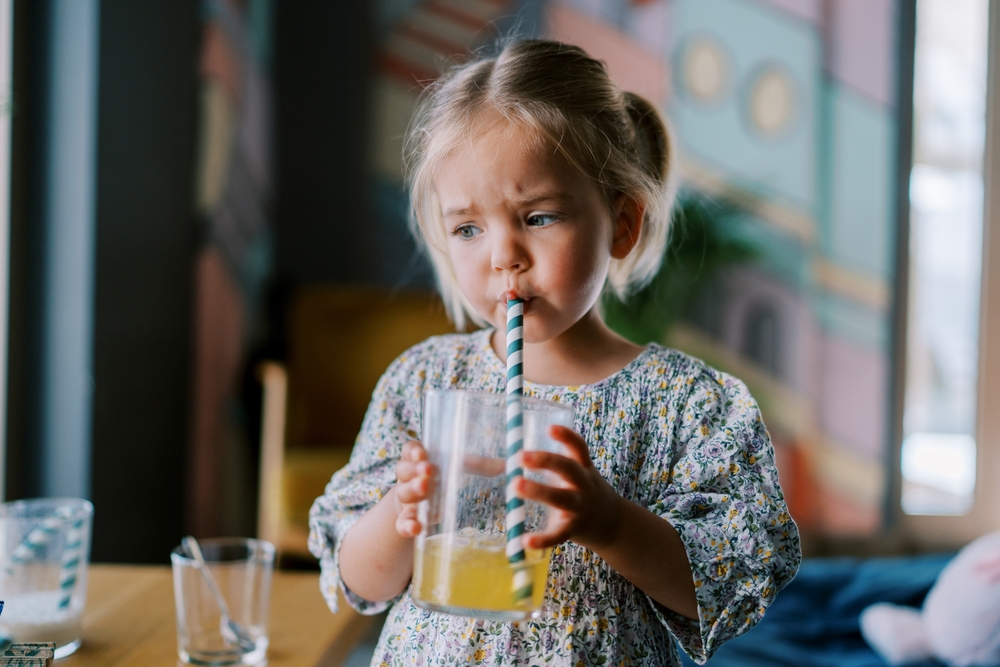 Little,Girl,Drinks,Juice,From,A,Glass,Through,A,Straw Cannucce biodegradabili per mense scolastiche